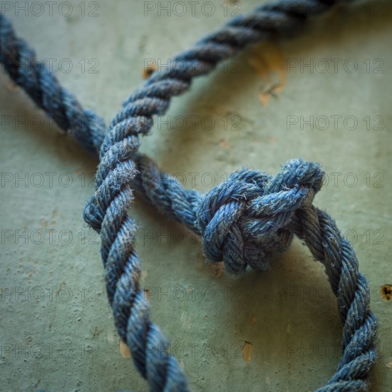 A close-up view reveals an intricately tied blue rope knot resting on a textured surface,
