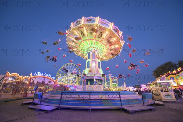 A chain carousel with lights turns at a fairground at dusk, chain carousel, spring festival,