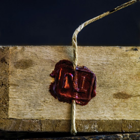 A wooden box is secured with twine, featuring a deep red wax seal that signifies authenticity and