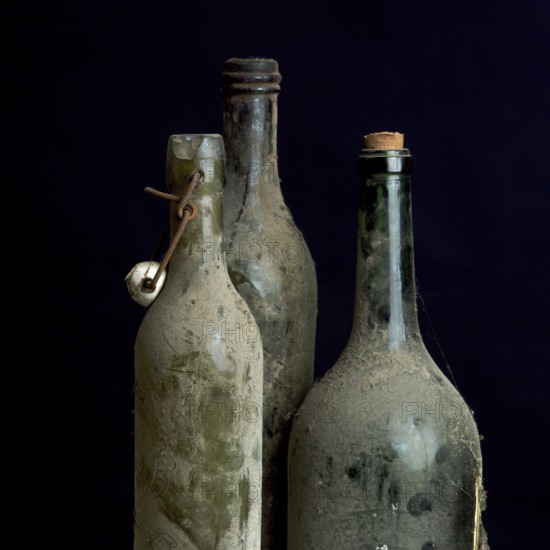 Three dusty vintage bottles stand together, covered in grime, highlighting their age and history.