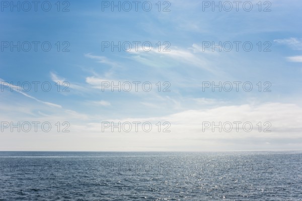 Dark ocean under a clear blue sky with bright white feathery clouds, cloud bank, horizon, water
