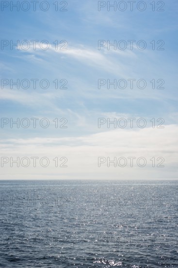Dark ocean under a clear blue sky with bright white feathery clouds, cloud bank, horizon, water