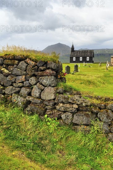 Traditional black church with cemetery, view through a stone wall to the wooden church Budakirkja,