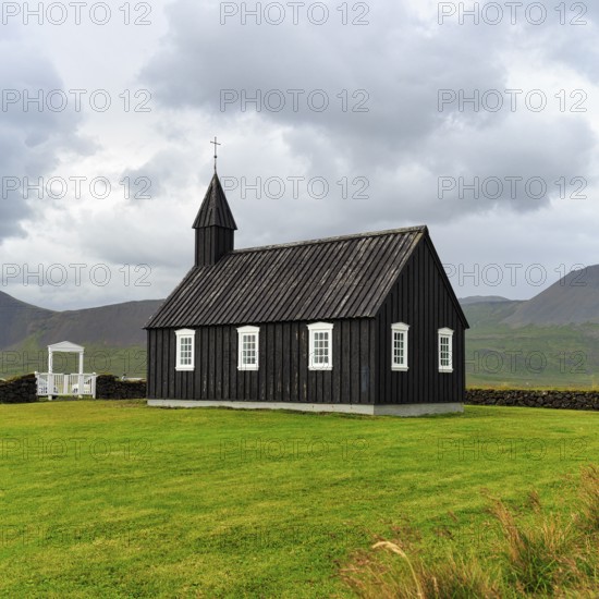 Traditional black church with white Tor tor in a meadow, wooden church Budakirkja, Búðir, Budir,