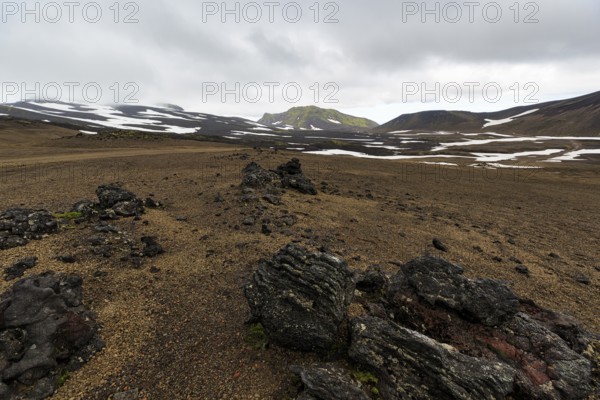 Barren volcanic landscape with snow fields, volcanic rock, mountain peaks with rain clouds,