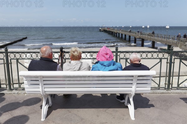 Holidaymakers sitting on a bench on the beach promenade, one is wearing strikingly colourful