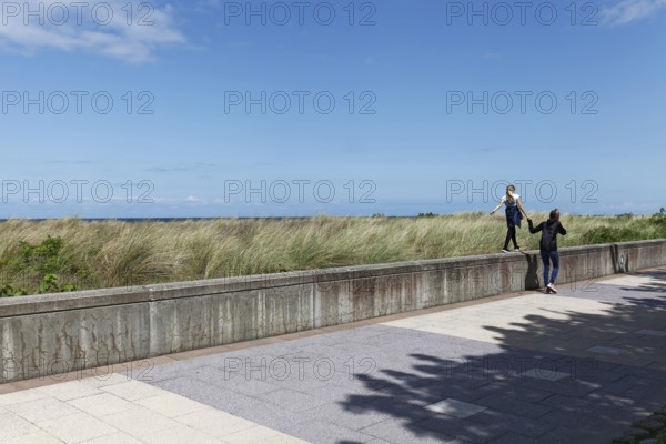 Teenager leads little girl by the hand over a wall on the beach promenade, Baltic resort