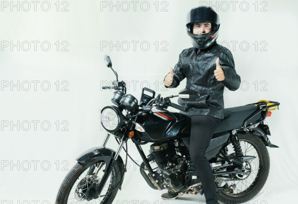 Smiling motorcyclist on his motorcycle with thumbs up, isolated. Motorcyclist with helmet on his