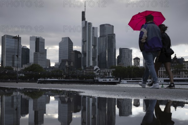 Two people walking in the rain under an umbrella in front of the Frankfurt bank skyline along the