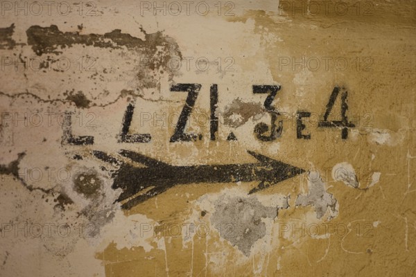 Lost Place, Ruin of a barracks, Patched wall with arrows and numbers in black on yellow, weathered