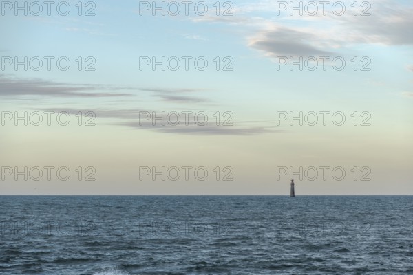 A lighthouse rises from the gentle waves of the ocean, surrounded by a tranquil seascape. Soft
