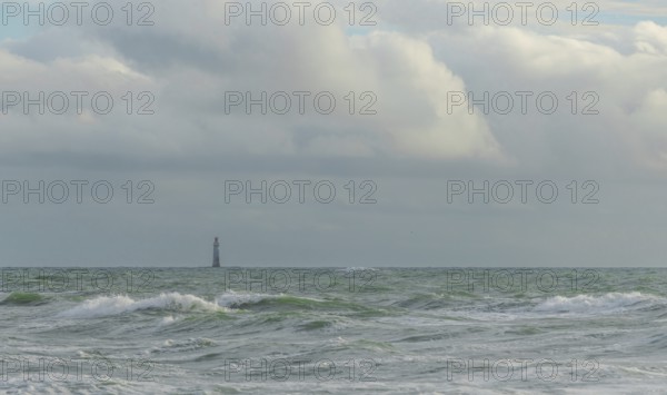Waves crash against the shore while a lone lighthouse looms in the distance under a sky filled with
