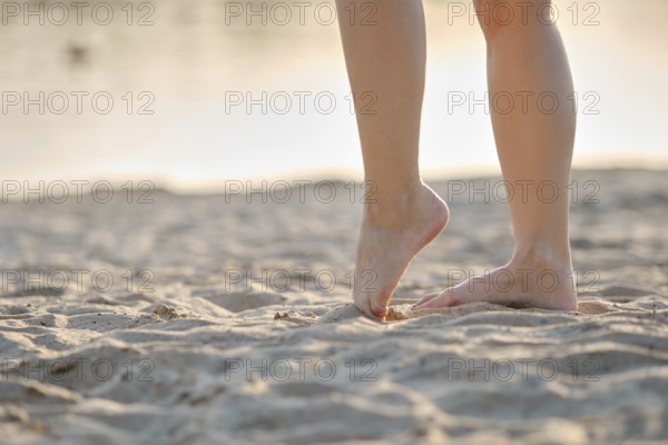 A person stands on soft, golden sand with bare feet, enjoying the warm texture as the sun sets in