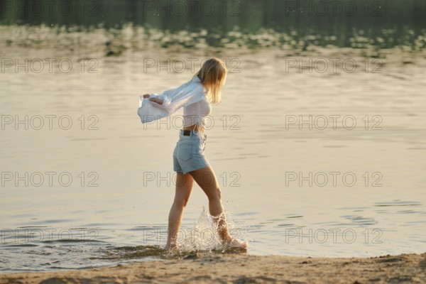 A young woman strolls through shallow water at a peaceful lakeshore creating splashes with her feet