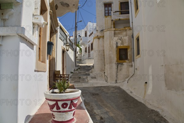 Narrow alley with white buildings and flower pot, old plaster, quiet and sunny atmosphere, Agia