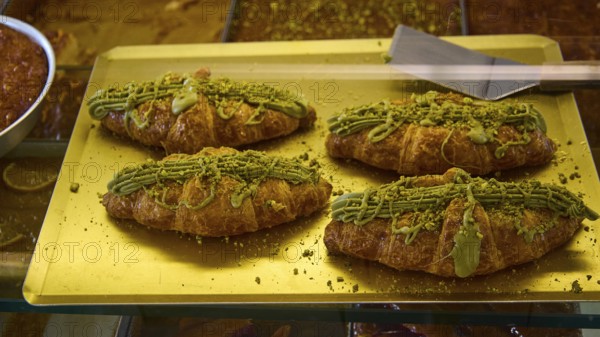 Four croissants decorated with pistachio cream on a golden tray, appetising and fresh, Agia Marina,