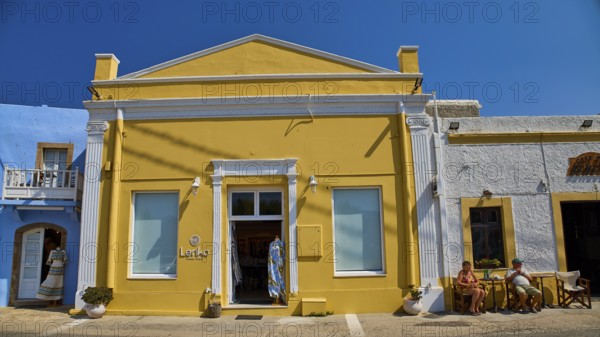 Yellow building with neoclassical facade, people in front of the door, clear blue sky, traditional