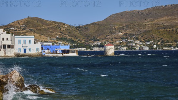 View of a coastal landscape with windmill, blue water and houses in front of hills, Agia Marina,