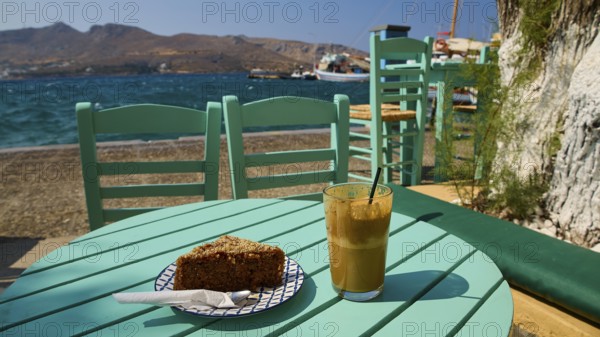 Turquoise-coloured table with drink and cake by the sea in sunny weather, relaxed atmosphere, Agia