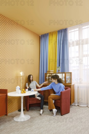 Two women are seated in a bright room, engaged in a lively discussion. One woman reaches out with a