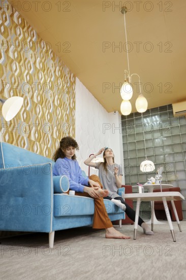 In a modern living room adorned with colorful wallpaper, two women are engaged in a fun skincare