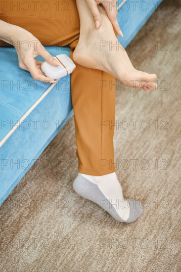 Unrecognizable woman use electric gadget to peel her heel from rough or dead skin while sitting on