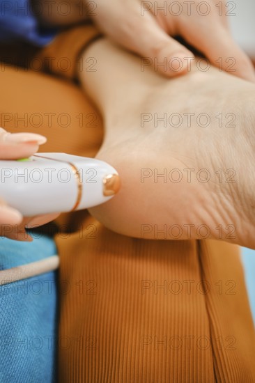 A woman is treating her foot with a device designed for removing rough skin. She sits comfortably