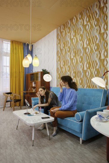 Two women sit comfortably on a bright blue sofa in a contemporary living room. They are engaged in
