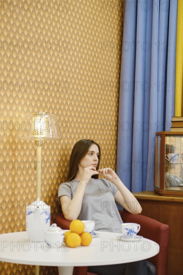 Young woman relaxing in a cozy living room with tea and fruit, surrounded by warm decor and soft