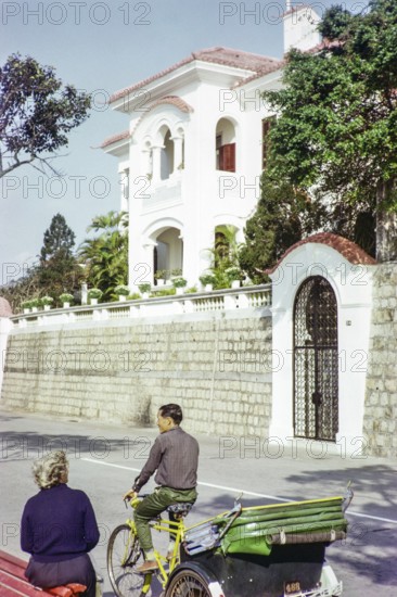 Tricycle rickshaw rider outside Portuguese colonial villa building, Avenida da Republica, Macau,