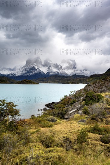 Cloudy mountain range Cuernos del Paine, shore of the blue lake Lago Pehoe in the evening light,