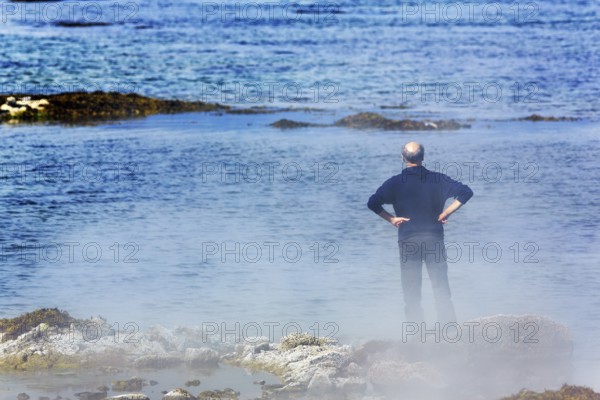 Hot spring flows into the sea, tourist on steaming rocky coast near Reykjanes, Súðavík,