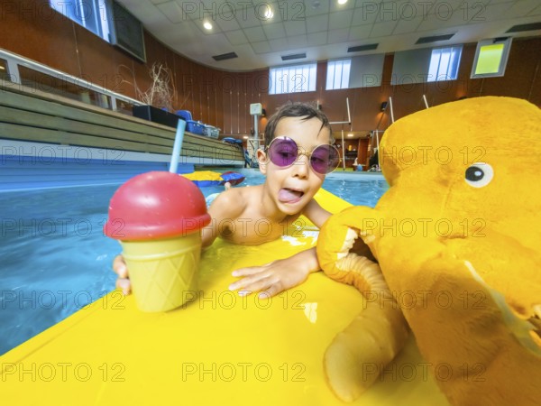 Boy with sunglasses sticking out his tongue, holding a refreshing drink and a plush toy while