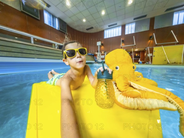 Young boy enjoys summer vacation, relaxing on a yellow float with a plush octopus and a refreshing