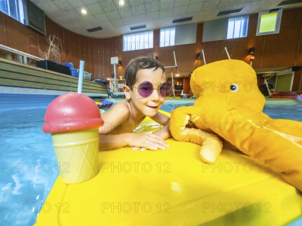 Young boy with sunglasses enjoying summer, playing with a plush octopus and an ice cream shaped toy