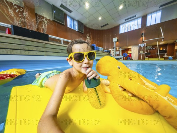 Young boy wearing sunglasses enjoying a refreshing drink while floating on a yellow raft with a