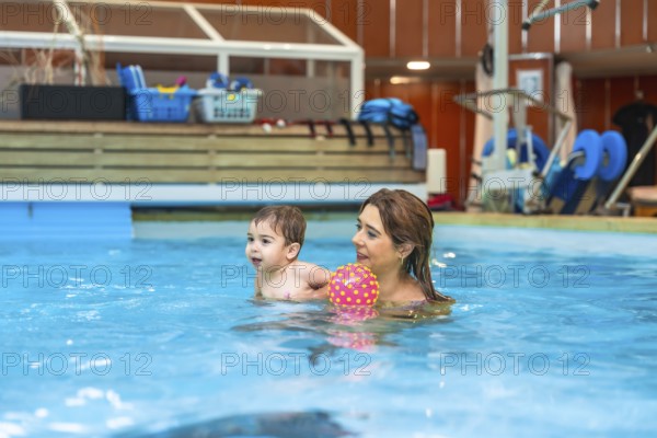 Mother and son having fun together playing with a colorful inflatable ball during a swimming lesson