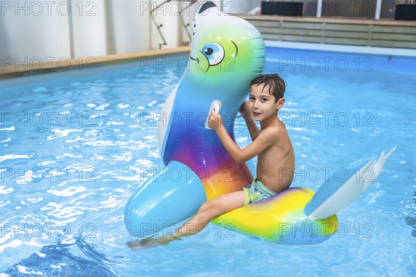 Boy enjoying summer holidays while riding an inflatable toy in a vibrant blue swimming pool,