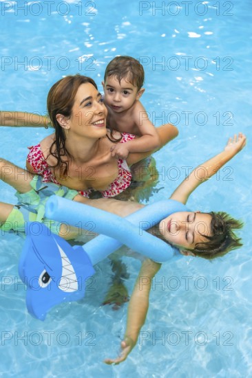 Mother and children enjoying summer vacation in a resort swimming pool, playing with inflatable