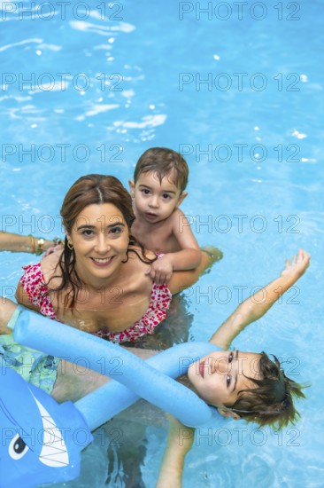Happy family enjoying sunny summer vacation in the pool, playing joyfully with inflatable toys and