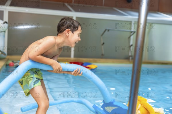 Happy boy playing with a pool noodle in an indoor swimming pool, relishing a fun summer activity