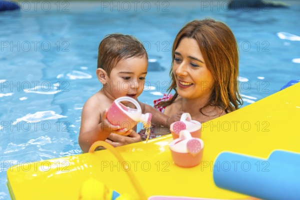 Mother and baby daughter enjoying time together, playing with pink and yellow toys while relaxing