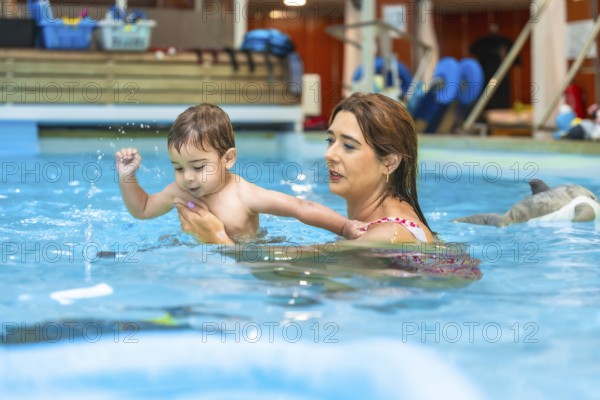 Swimming instructor holding baby swimming in indoor pool during a lesson, promoting water safety