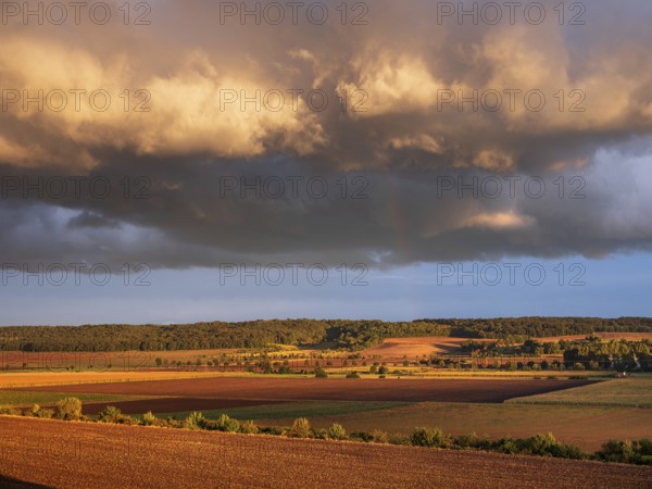 Field landscape in autumn, ploughed fields under dark storm clouds with rainbow in the evening