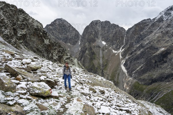 Mountaineer on steep rocky mountain landscape with fresh snow in summer, behind mountain peaks