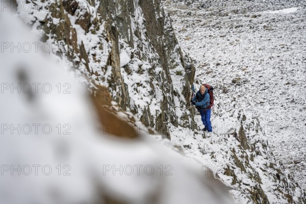 Mountaineer on a rope-secured path in a steep, rocky mountain landscape with fresh snow in summer,
