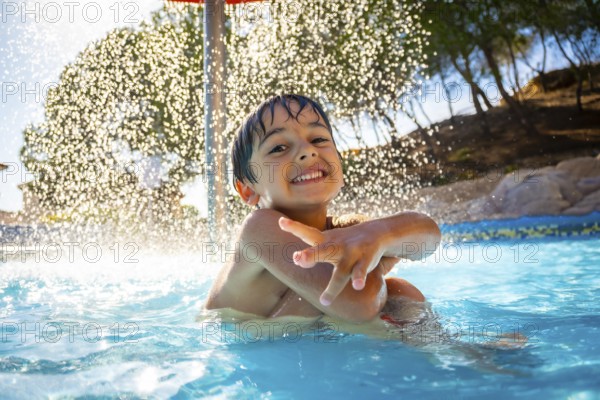 Smiling boy enjoying playful moments under a refreshing water shower in a swimming pool on a