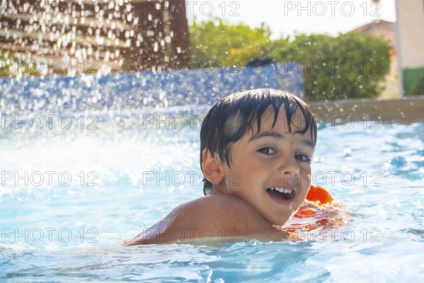Smiling child enjoying summer vacations playing in a blue swimming pool with inflatable armbands