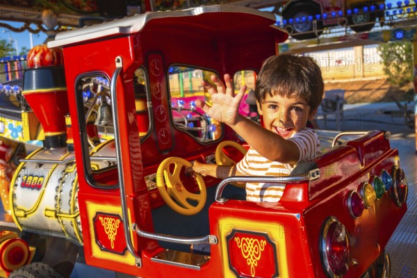 Smiling child enjoying a ride on a vibrant amusement park train, waving enthusiastically. Bright
