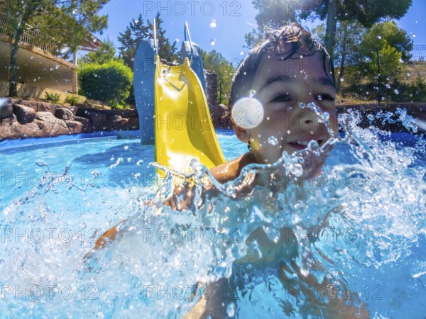 Young boy having fun going down a water slide and splashing into a refreshing pool on a sunny